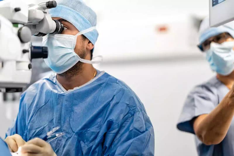 Chirurgien ophtalmologue au bloc opératoire utilisant un microscope pour une chirurgie réfractive intraoculaire (implants).