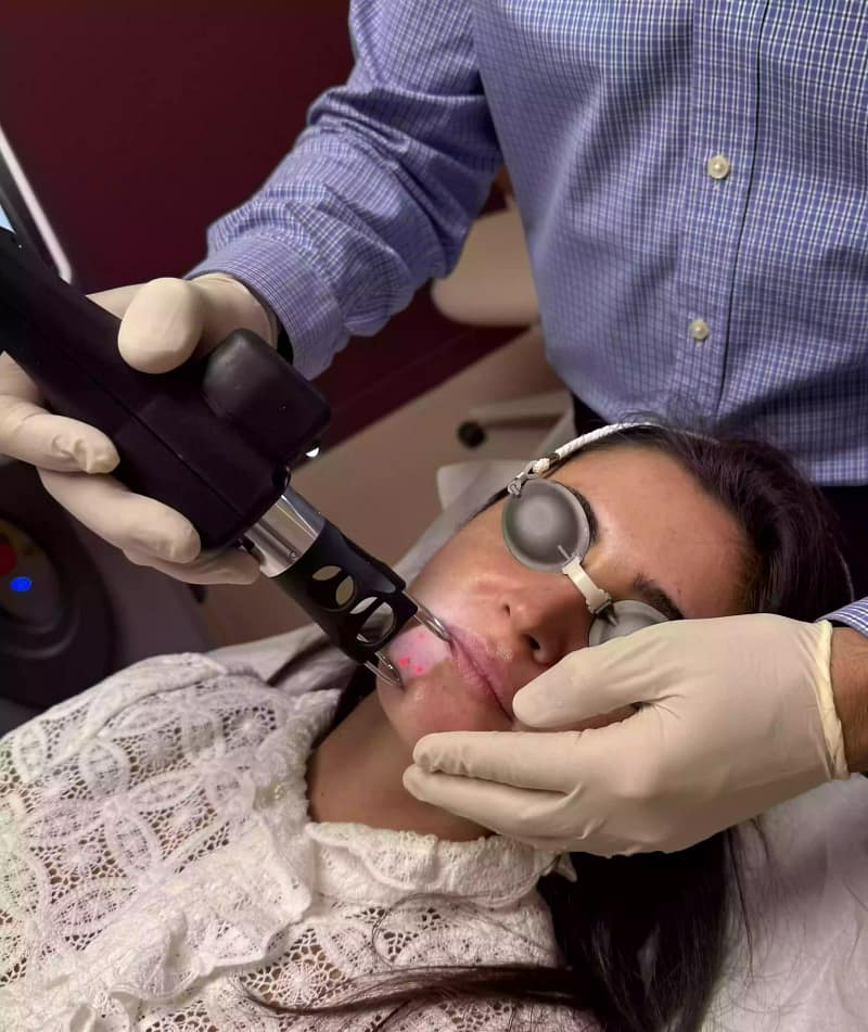 Séance de laser CO₂ médical : un praticien applique le laser sur le visage d’une patiente protégée par des coques oculaires.
